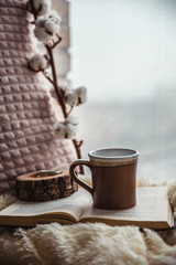 Details of still life in the home interior. Beautiful tea Cup, cut wood, book and pillows, cotton flower on a windowsill. Vintage, rustic. Cosy autumn-winter concept. Copy space