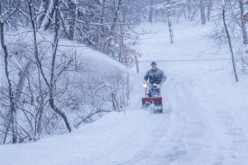 An old white man is using snow blower to plow / blow snow 