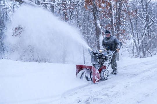 An old white man is using snow blower to plow / blow snow 