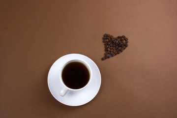 top view of black coffee cup and heart with coffee beans on brown background