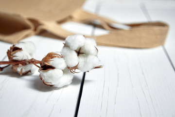 Natural cotton flowers. Plant and reusable shopping bag lie on a white wooden table. Selective focus