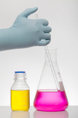 A hand in laboratory gloves mixes chemistry. Liquid in laboratory bottles. Scientific biochemical...