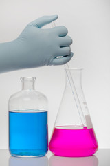 A hand in laboratory gloves mixes chemistry. Liquid in laboratory bottles. Scientific biochemical laboratory. Colorful liquid.