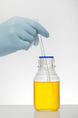 A hand in laboratory gloves mixes chemistry. Liquid in laboratory bottles. Scientific biochemical laboratory. Colorful liquid.