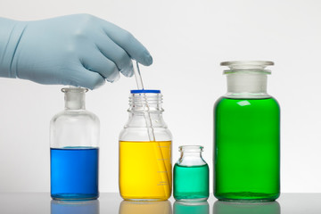 A hand in laboratory gloves mixes chemistry. Liquid in laboratory bottles. Scientific biochemical laboratory. Colorful liquid.