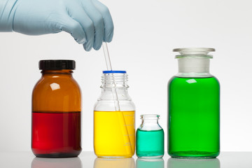 A hand in laboratory gloves mixes chemistry. Liquid in laboratory bottles. Scientific biochemical laboratory. Colorful liquid.