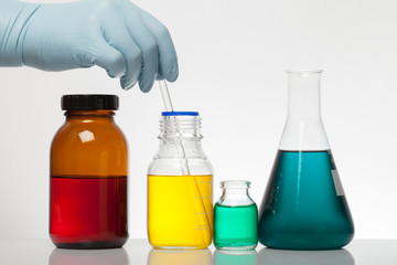 A hand in laboratory gloves mixes chemistry. Liquid in laboratory bottles. Scientific biochemical laboratory. Colorful liquid.