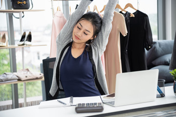 Asian creative designer stretching arms and close eye in front of laptop computer on work desk