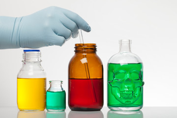 A hand in laboratory gloves mixes chemistry. Liquid in laboratory bottles. Scientific biochemical laboratory. Colorful liquid.