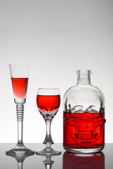 A skull bottle and crystal glasses with a liquid, alcohol drink.