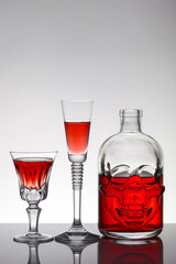 A skull bottle and crystal glasses with a liquid, alcohol drink.