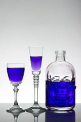 A skull bottle and crystal glasses with a liquid, alcohol drink.