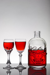 A skull bottle and crystal glasses with a liquid, alcohol drink.