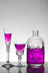 A skull bottle and crystal glasses with a liquid, alcohol drink.