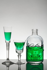 A skull bottle and crystal glasses with a liquid, alcohol drink.