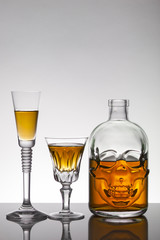 A skull bottle and crystal glasses with a liquid, alcohol drink.
