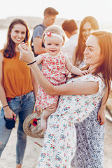 happy stylish mom playing with joyful daughter and cuddling, relaxing with friends on summer...