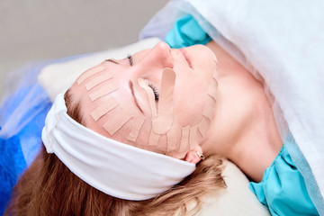 Taping. Facial skin care. Physiotherapy and cosmetology procedure. Young woman lying with tape on her face. Method of non-surgical skin rejuvenation