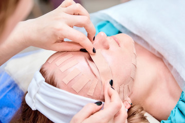 Obraz na płótnie Canvas Taping. Facial treatment. Young woman lying with tape on her face. Physiotherapy and cosmetology procedure. Method of non-surgical skin rejuvenation.