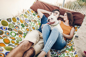 Cute dog smiling while on a trip with his owners, joyful young family, man and woman lying in comfortable hammock on a beach