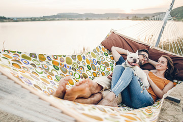 Hipster family on vacation concept, happy woman and man relaxing on a hammock at the beach with...