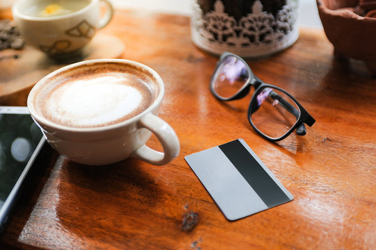 Cappuccino coffee in white cup lay on wooden table with smartphone and credit card,Relax time with coffee,Art of coffee,Online shopping