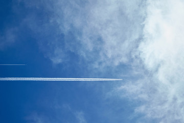 Two planes in the blue sky with white clouds. The aircraft leaves traces