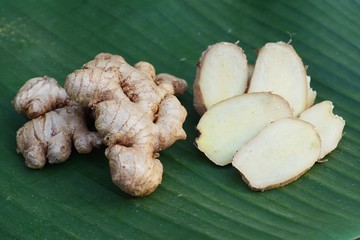 Fresh ginger root and ginger sliced on green leaf background on wood table background, tropical...