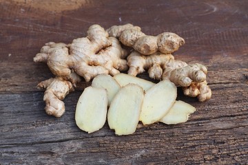 Fresh ginger root and ginger sliced on green leaf background on wood table background, tropical...