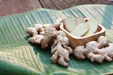 Fresh ginger root and ginger sliced on green leaf background on wood table background, tropical herb concept