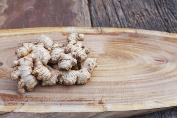 Fresh ginger root and ginger sliced on green leaf background on wood table background, tropical herb concept