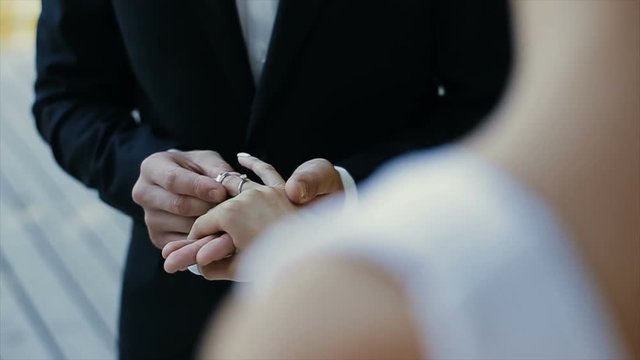 The groom puts the wedding ring on finger of the bride and kisses her hand. The bride and groom exchange wedding rings.