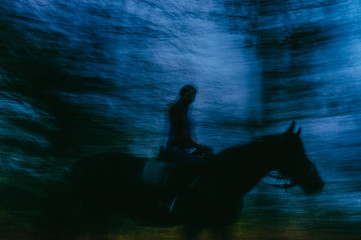 A Blurred Silhouette of An Equestrian on Horseback in the Dark Forest at the Night