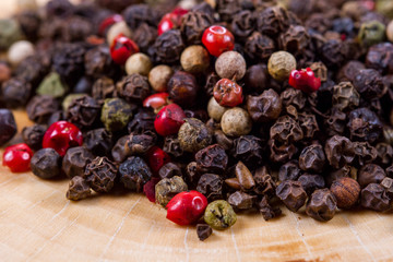 Black, white and red pepper peas on a wooden background