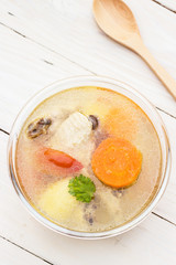  Bowl of chicken soup and chicken wings with carrots, potatoes and tomatoes on wood table with wooden spoon