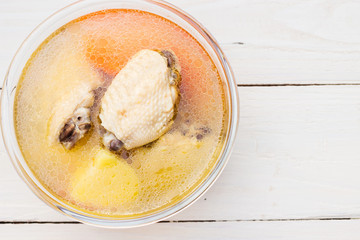  Bowl of chicken soup and chicken wings with carrots, potatoes and tomatoes on wood table 