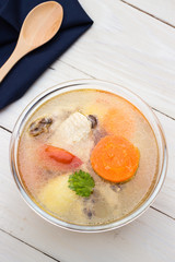 Bowl of chicken soup and chicken wings with carrots, potatoes and tomatoes on gray table mat with wooden spoon