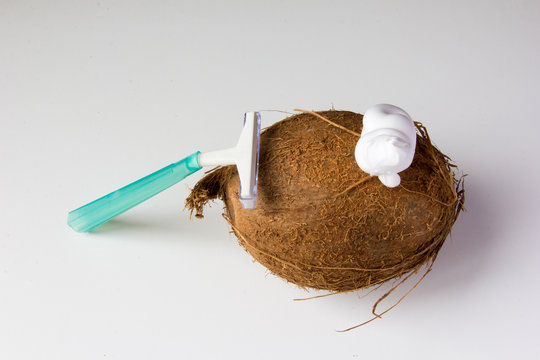 Abstract picture meaning epilation procedure. Hairy coconut with a foam and plastic green razor at white background