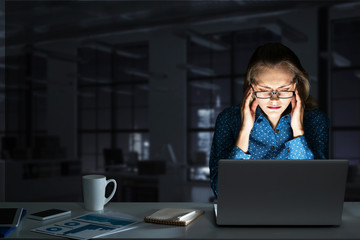 Attractive blonde working on laptop in dark office. Mixed media