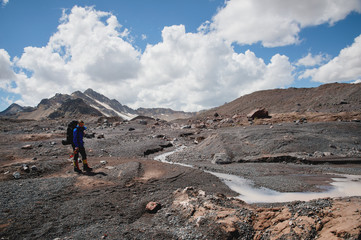 A mountaineer with a backpack walks in crampons walking along a dusty glacier with sidewalks in the...