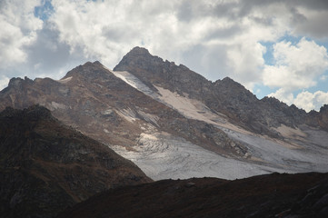 Mountain landscape dusty dirty volcanic slope with a cracked melting glacier against the backdrop of the Caucasus Mountains. Global warming. Glaciers of the North Caucasus