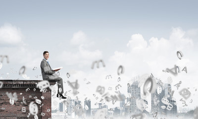 Fototapeta premium Man on roof edge reading book and symbols flying around