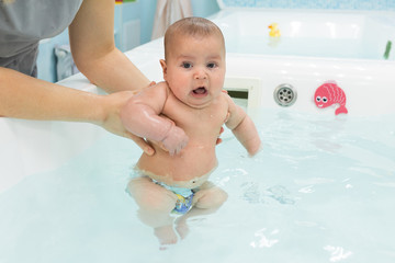 Cute baby swimming in bathroom. The instructor teaches mom infants fitness and swimming