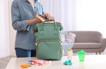 Woman packing baby accessories into maternity backpack on table indoors, closeup