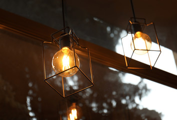 Pendant lamps with glowing light bulbs near window indoors