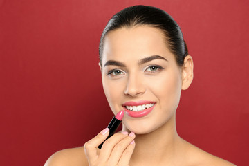 Young woman applying lipstick on color background