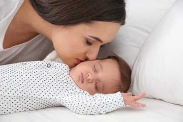 Obraz na płótnie Canvas Woman kissing her sleeping baby on bed