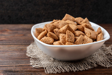 Dried breakfast pads in white bowl on dark wooden background.