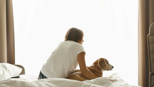 Woman sitting on bed with dog near her and hugging him