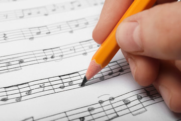 Woman writing music notes on sheet with pencil, closeup